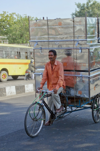 An Indian man carries metal trunks on his rickshaw.