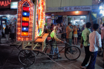 A rickshaw carrying a lighted decoration follows a wedding procession in India.