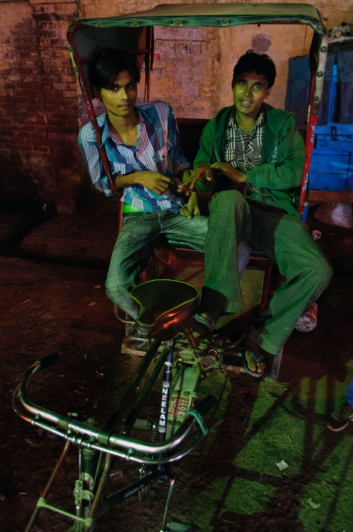 Two Indians sit in a rickshaw during the evening hours.