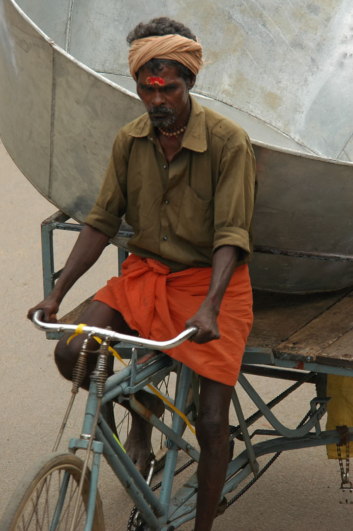 A South Indian man pedals his overloaded rickshaw.