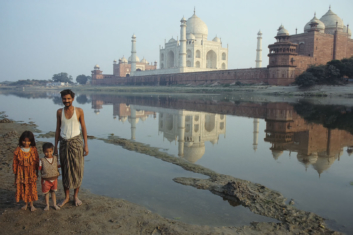 A family poses on the other side of the river from the taj mahal