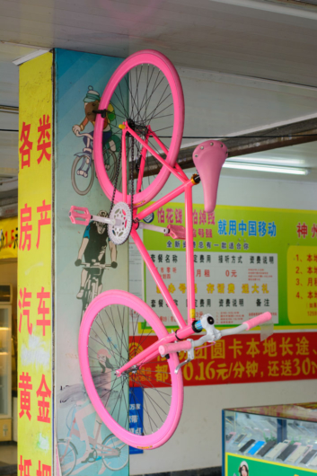 A pink bike hangs on a wall in a Chinese store.