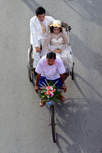 A fancy dressed couple sit in a rickshaw in a parade in Thailand.
