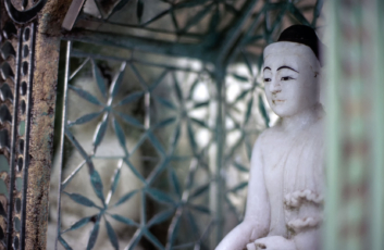A white Buddha stands in front of a silver background in Myanmar.