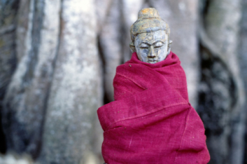 A small stone Buddha statue is wrapped in red cloth in Myanmar.