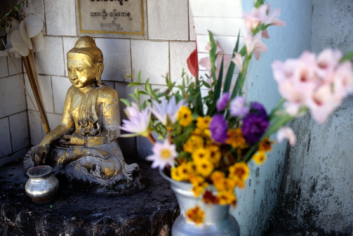 A post of flowers stands next to a Buddha statue in Myanmar.