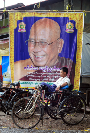 A rickshaw is parked beneath the banner of a monk in Myanmar.
