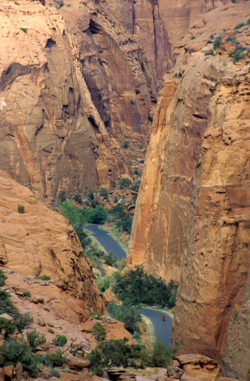 A small red cyclist pedals through a canyon.