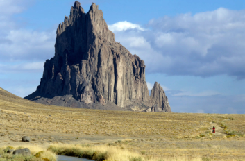 A little red cyclist pedals past Shiprock.