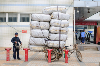 A Chinese man stands next to an overloaded cargo bike.
