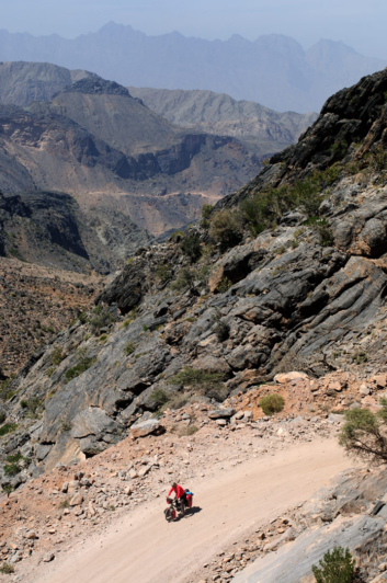 Touring bicyclist heads down a mountain dirt road in Oman.