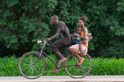 An African bicycle taxi speeds on it's way carrying a woman with her child.