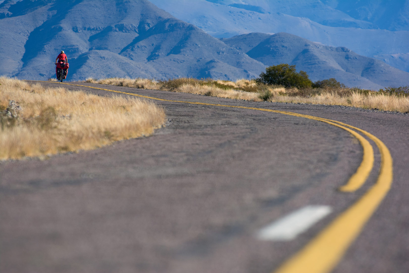 A small red cyclist heads towards the mountains in Northern Argentina.