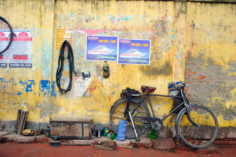 A bicycle is parked against a yellow wall in Bangladesh.