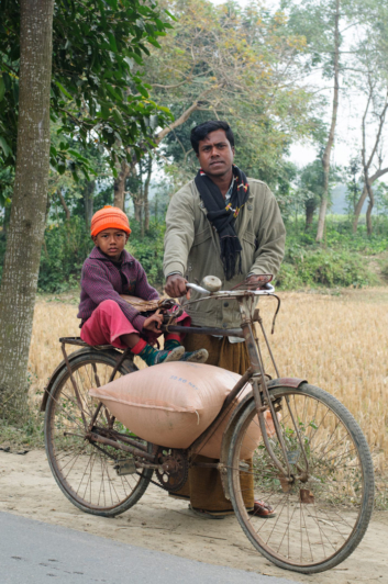 A Bangladeshi father holds his bicycle while his son sits on the back rack.