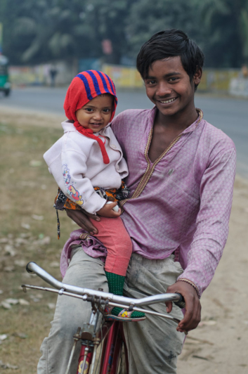 A boy carries his younger brother while sitting on a bike in Bangladesh.