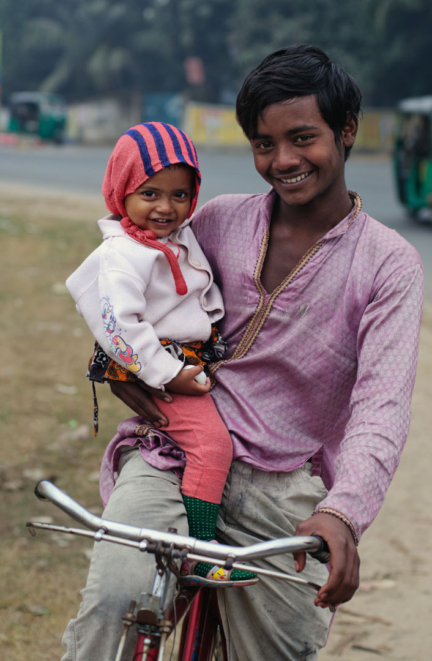A boy sits on a bicycle while holding a younger brother in Bangladesh.