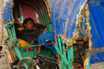 A chauffeur sleeps between 2 rickshaws in Dhaka, Bangladesh.