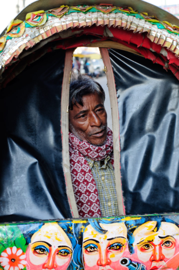 a rickshaw chauffeur peers through the canvas awning opening in Dhaka.