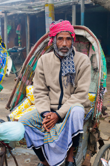 A rickshaw chauffeur sits proudly while dressed in warm winter clothes in Bangladesh.