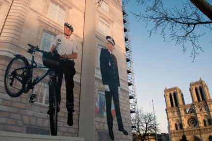 A policeman stands next to a bike on a wall hanging in Paris.
