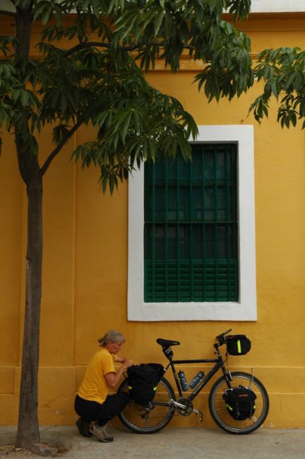 Closing a back bicycle pannier in front of a yellow building in Pondicherry, India.